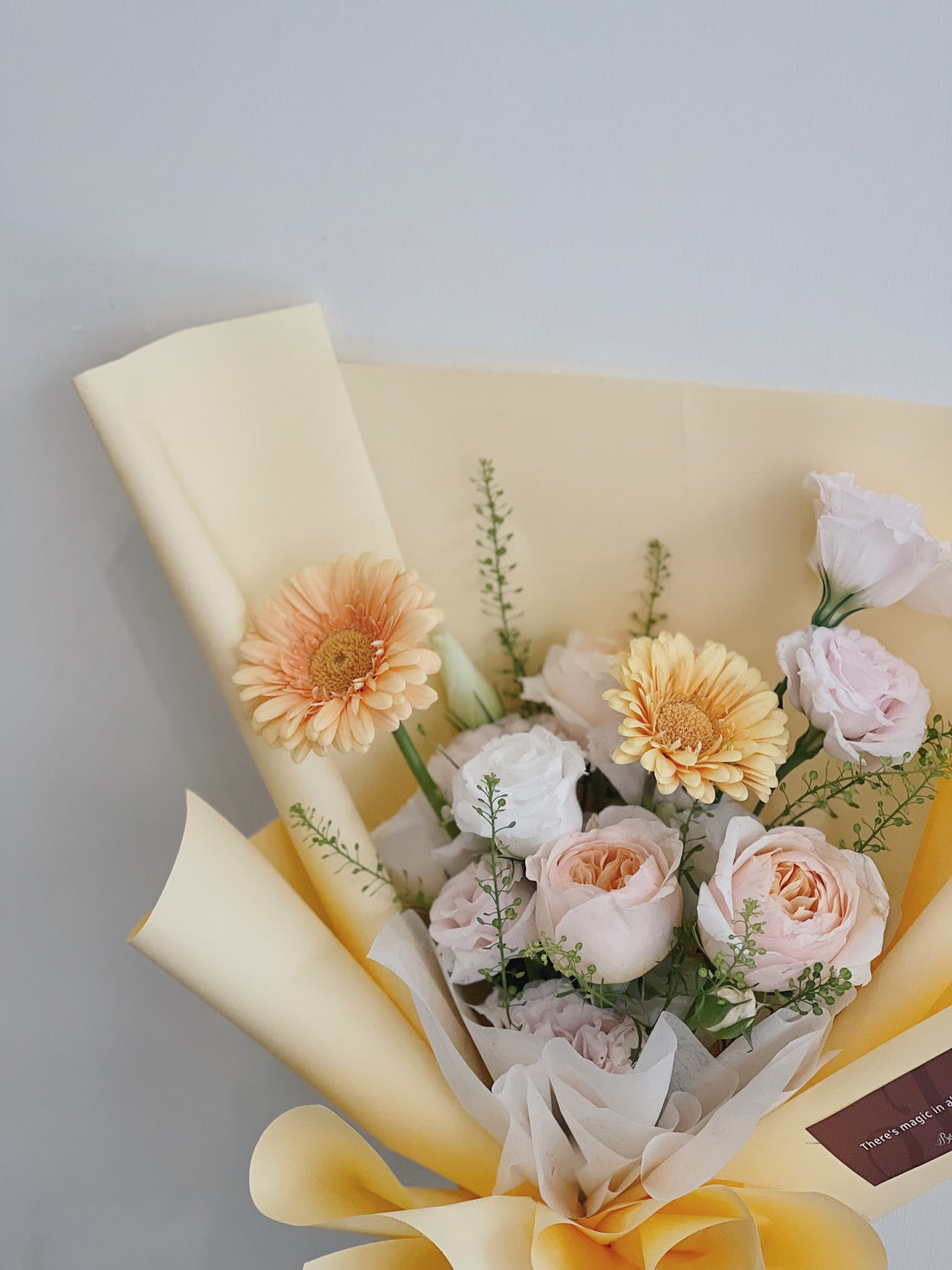 黃色和白色包裝的鮮花花束,包含桃色玫瑰和橙色非洲菊。