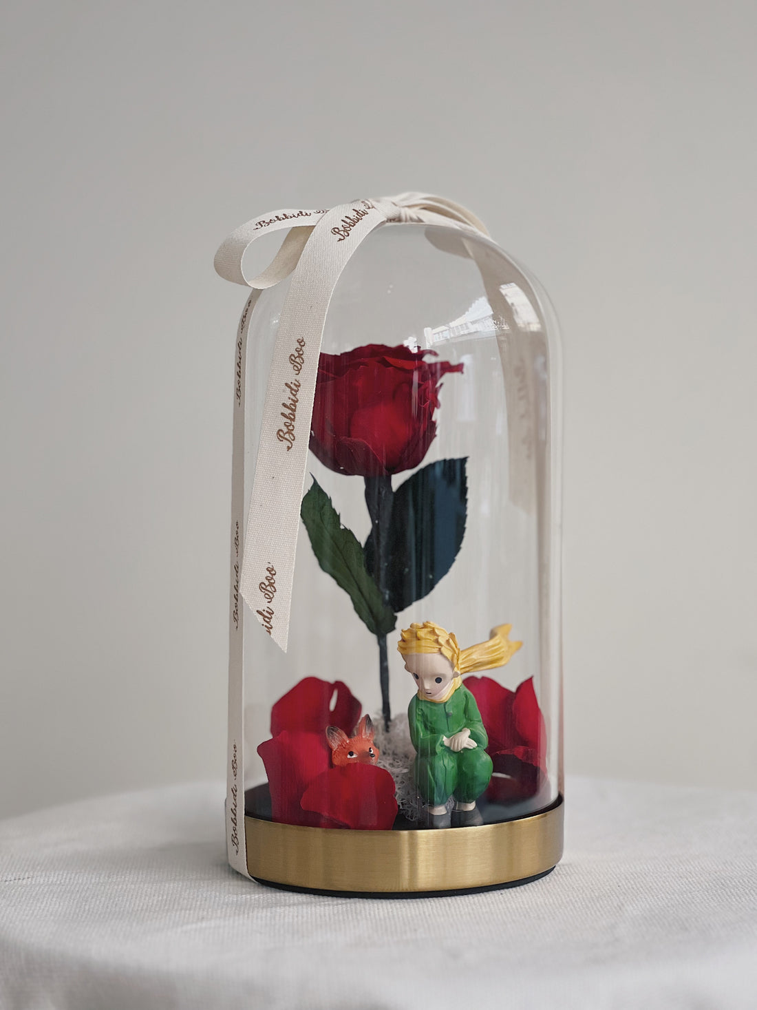 紅玫瑰在玻璃罩內,小王子與狐狸雕像在旁。
