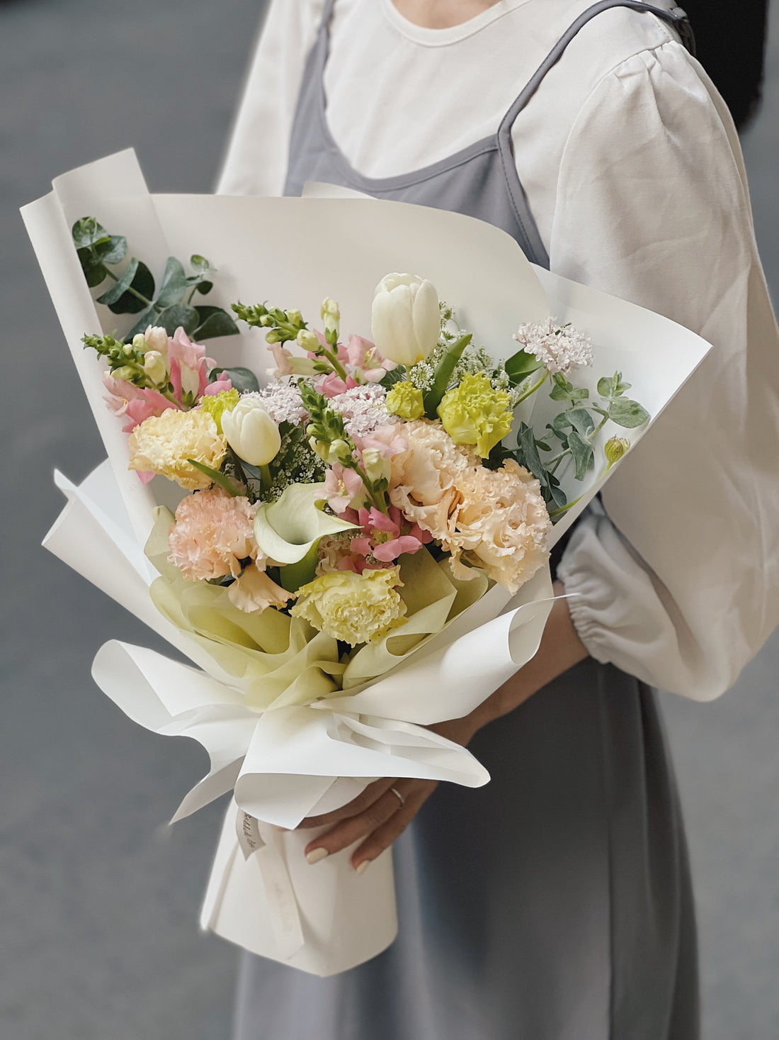 女子手捧花束，內含白色與粉色花朵，配有綠葉襯托。