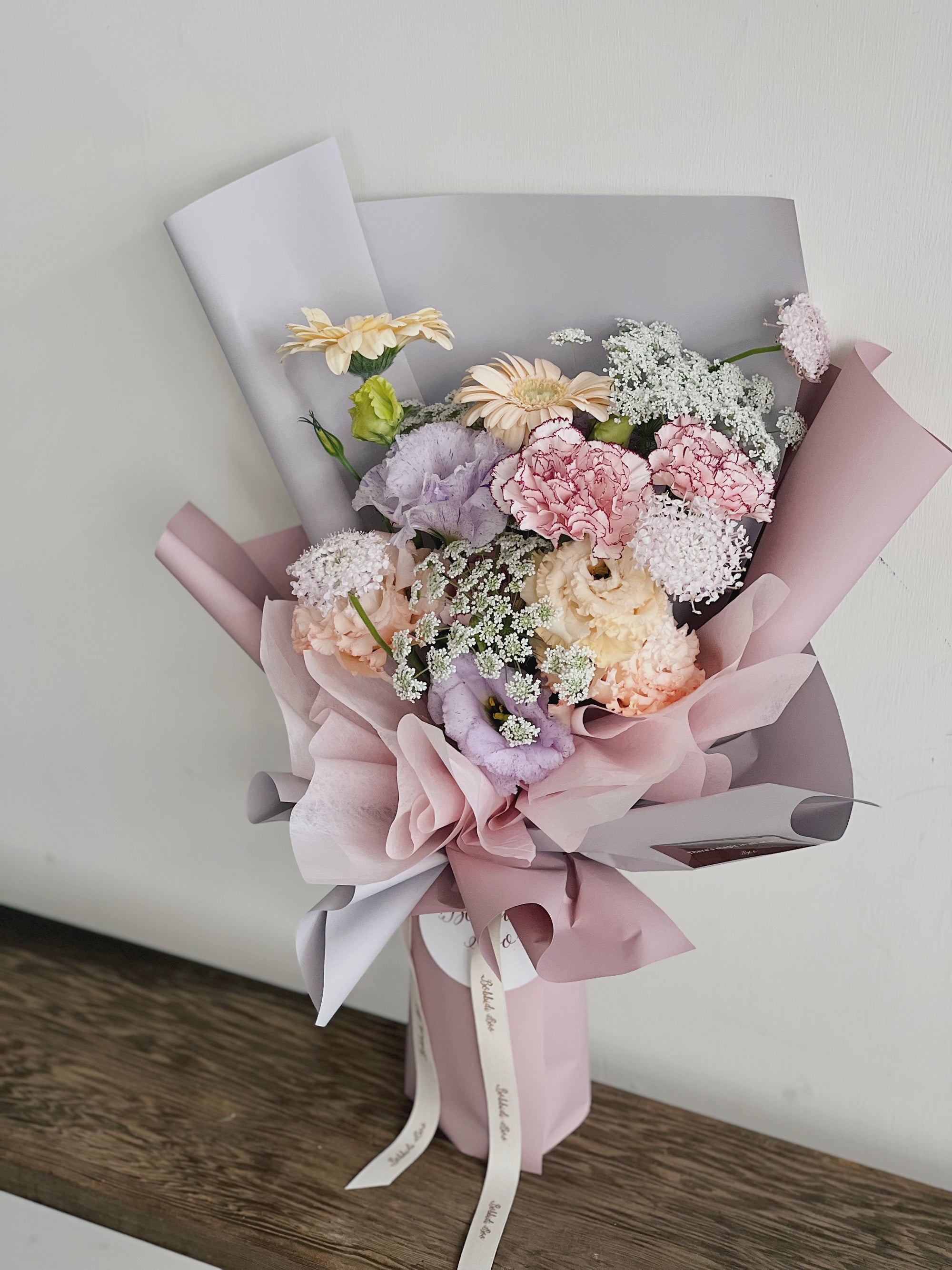 粉色包裝的鮮花花束，包含康乃馨、繡球花和滿天星。