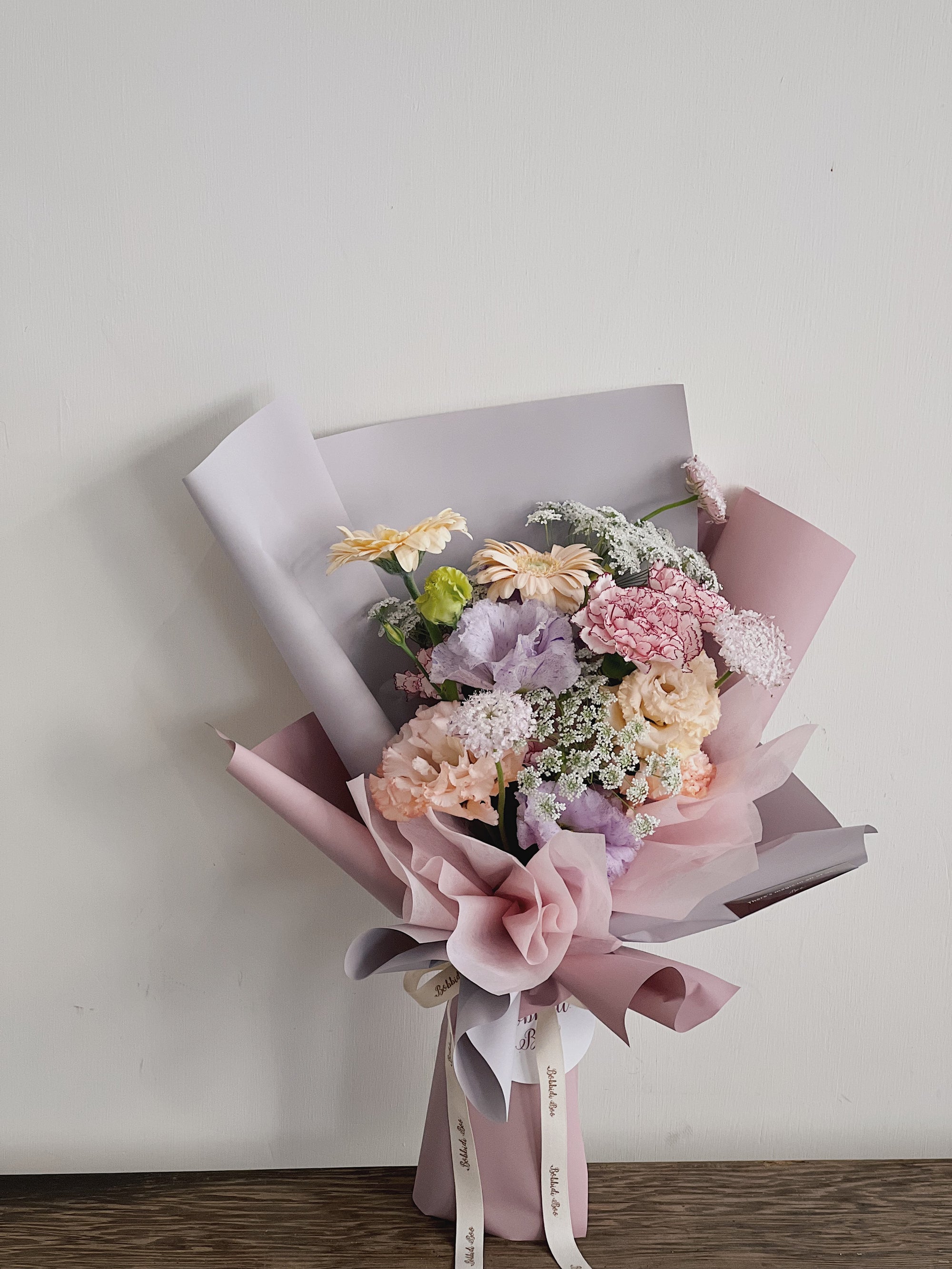 粉色及紫色花束，包裝精美，包含康乃馨和雛菊。