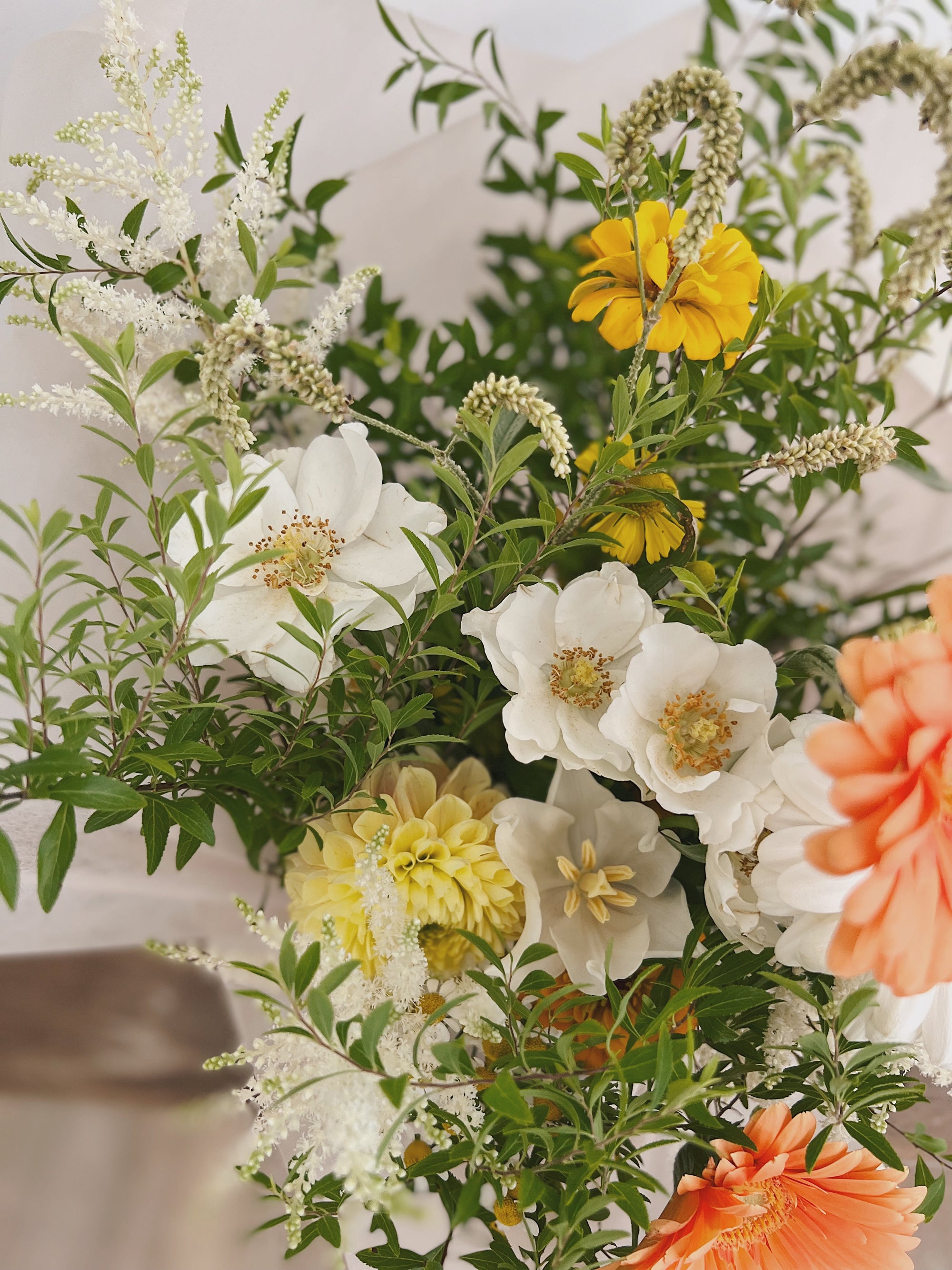 白色、黃色和橙色花組成的鮮花花束，綠葉點綴。