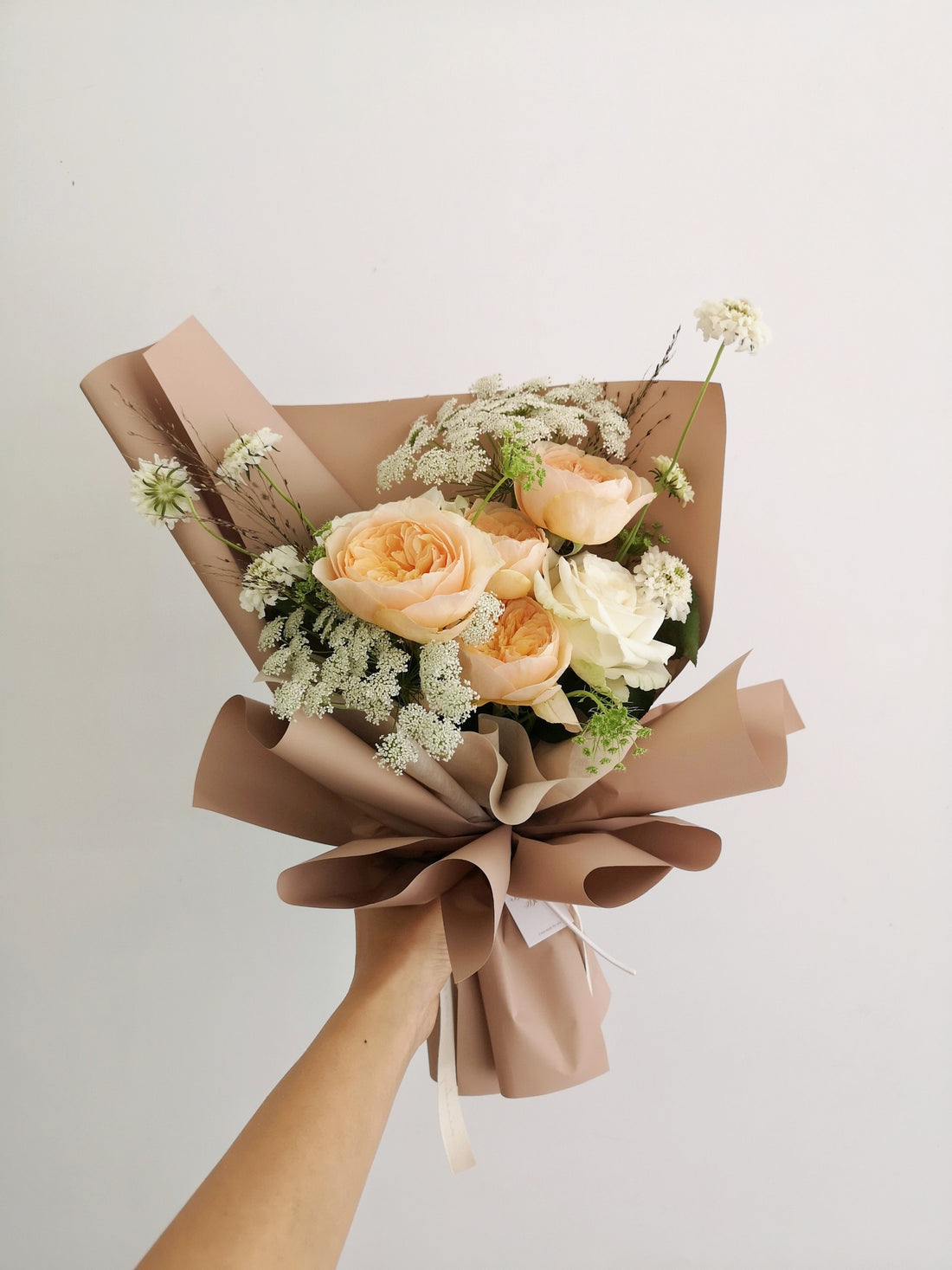 一束白色和淺黃色花卉的花束，用米色包裝紙包裹，放置在木架上。