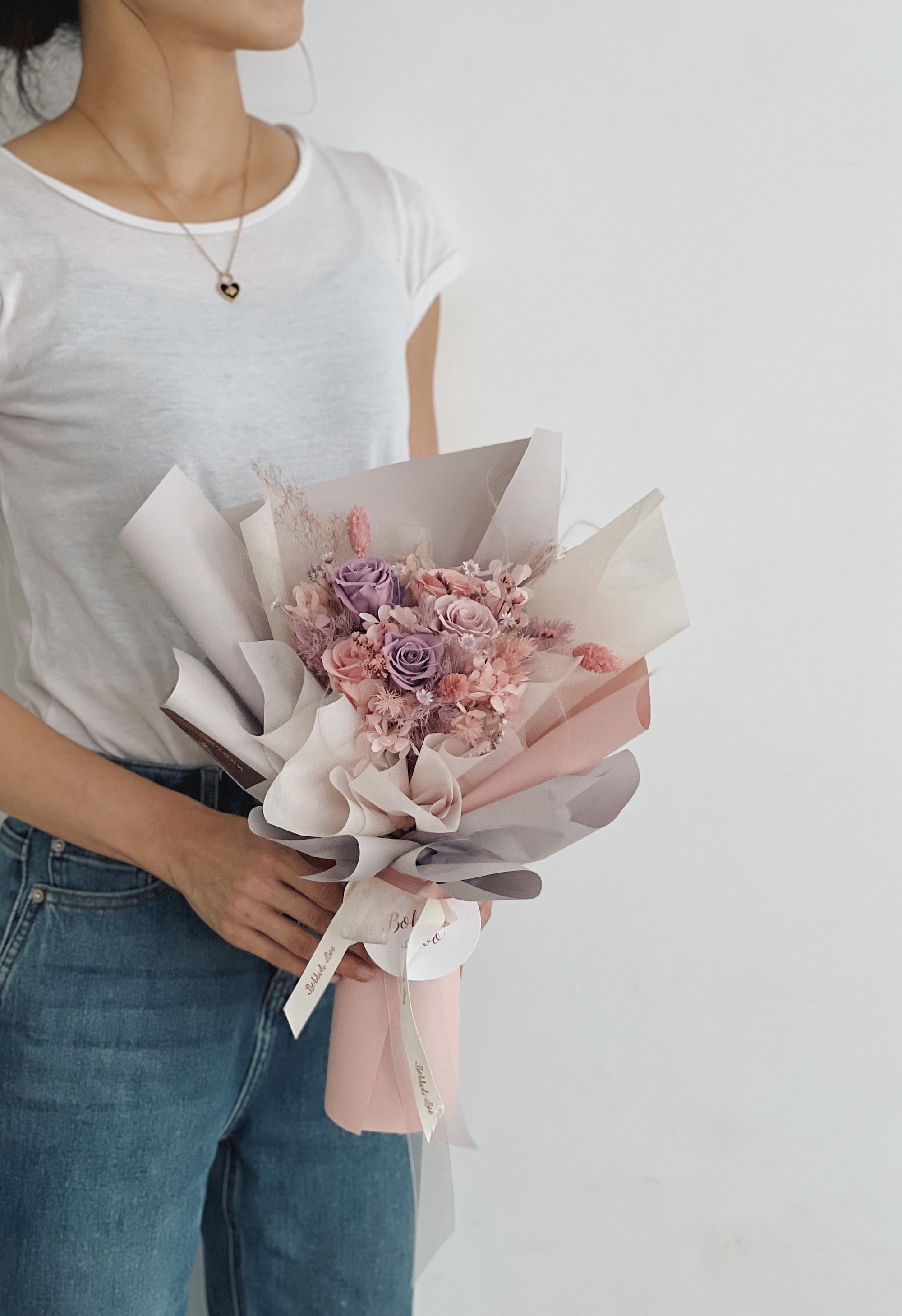 一位女性手持永生玫瑰花花束，花色柔和，包裝精美。