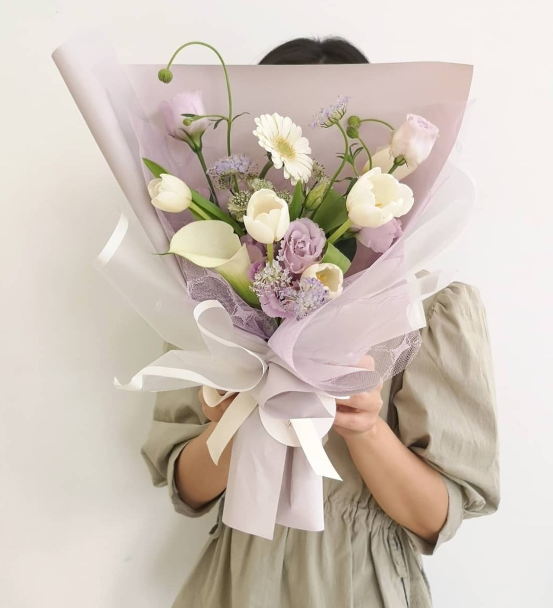 一位穿灰色衣服的女性拿著一束鬱金香花束。