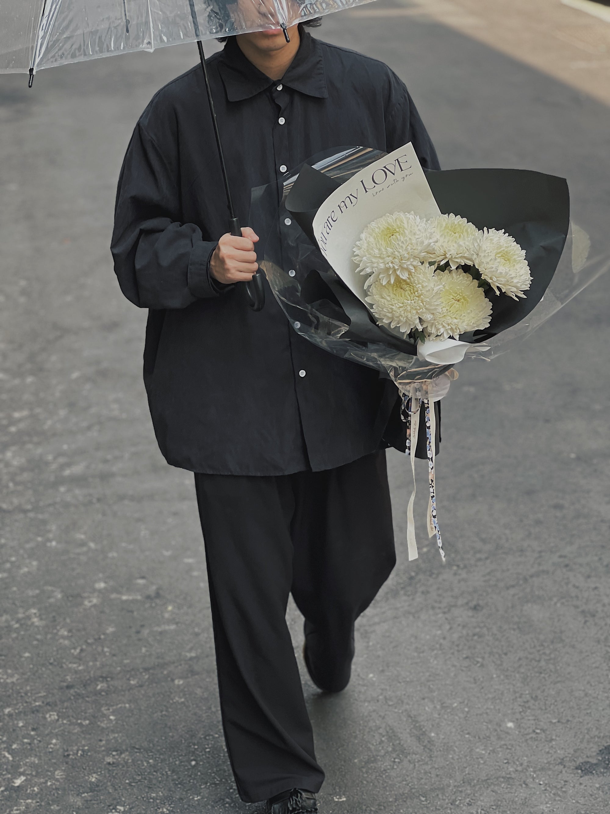 一名穿黑衣的人撐傘，手持白色菊花花束。