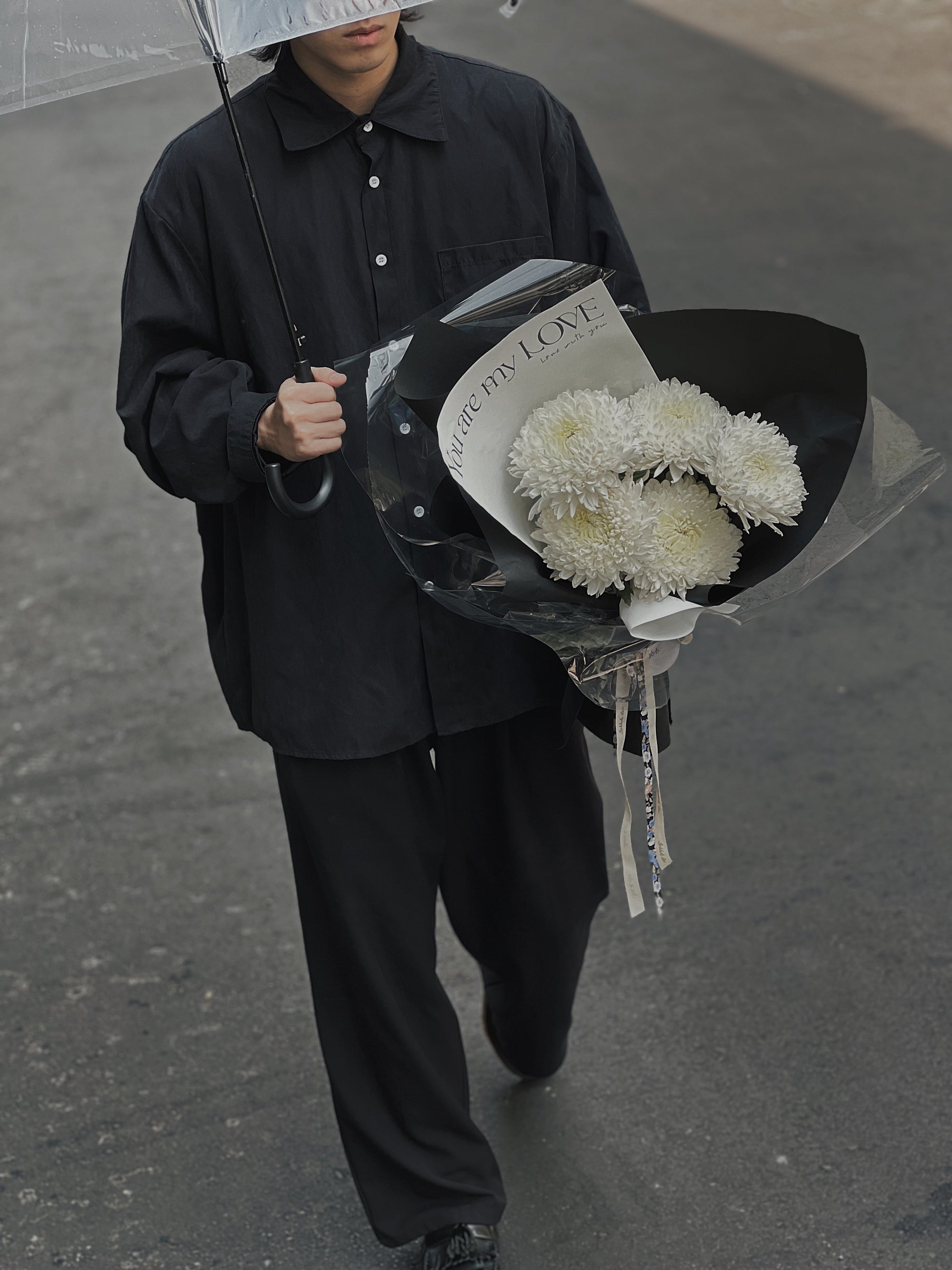 一位男子撐傘，手持白色菊花花束。