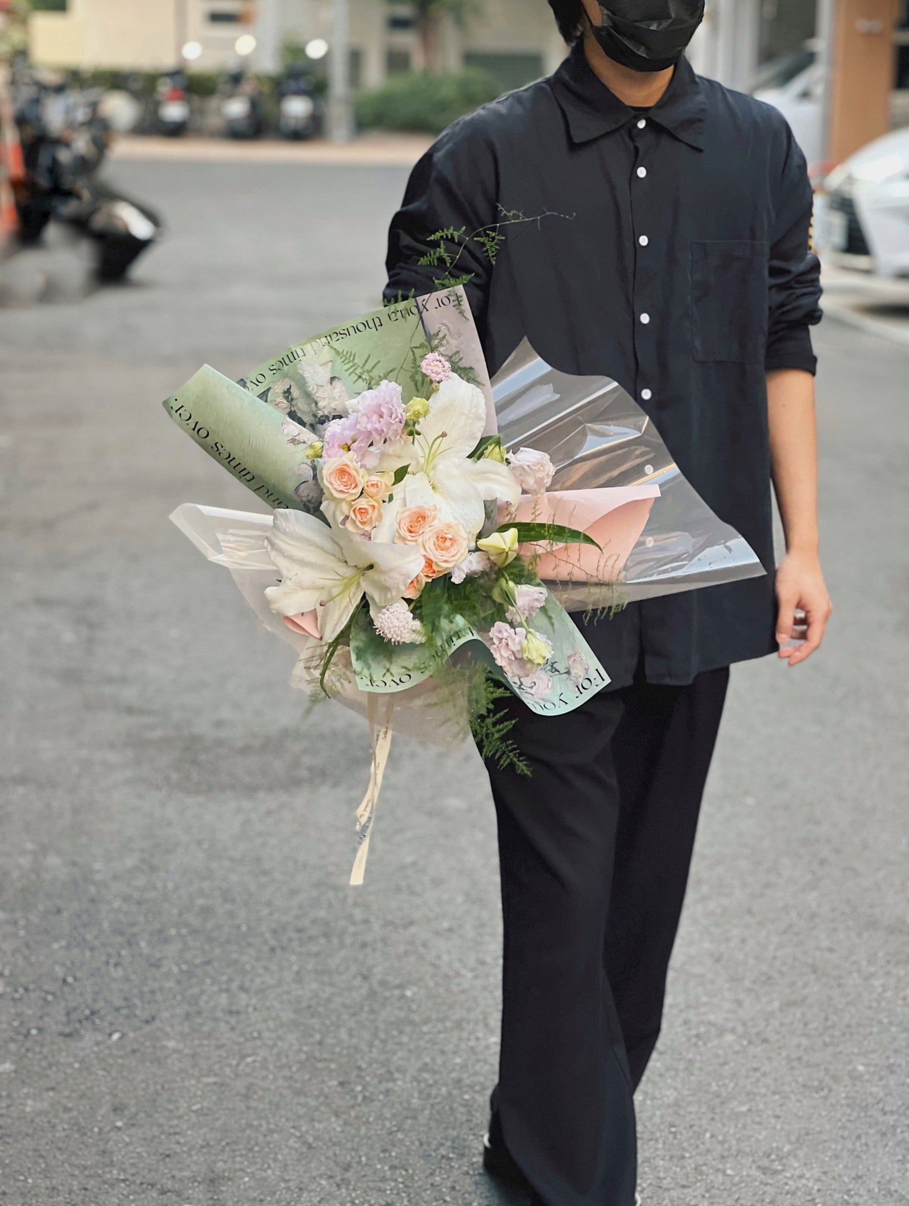 穿著黑衣的人手持綠色包裝的百合花花束。