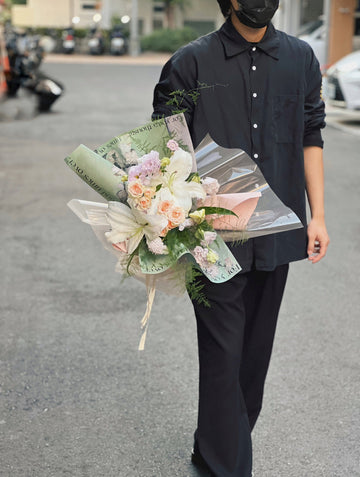 穿著黑衣的人手持綠色包裝的百合花花束。