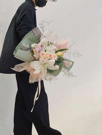 一位穿著黑色衣物的人拿著綠色包裝的百合花花束。