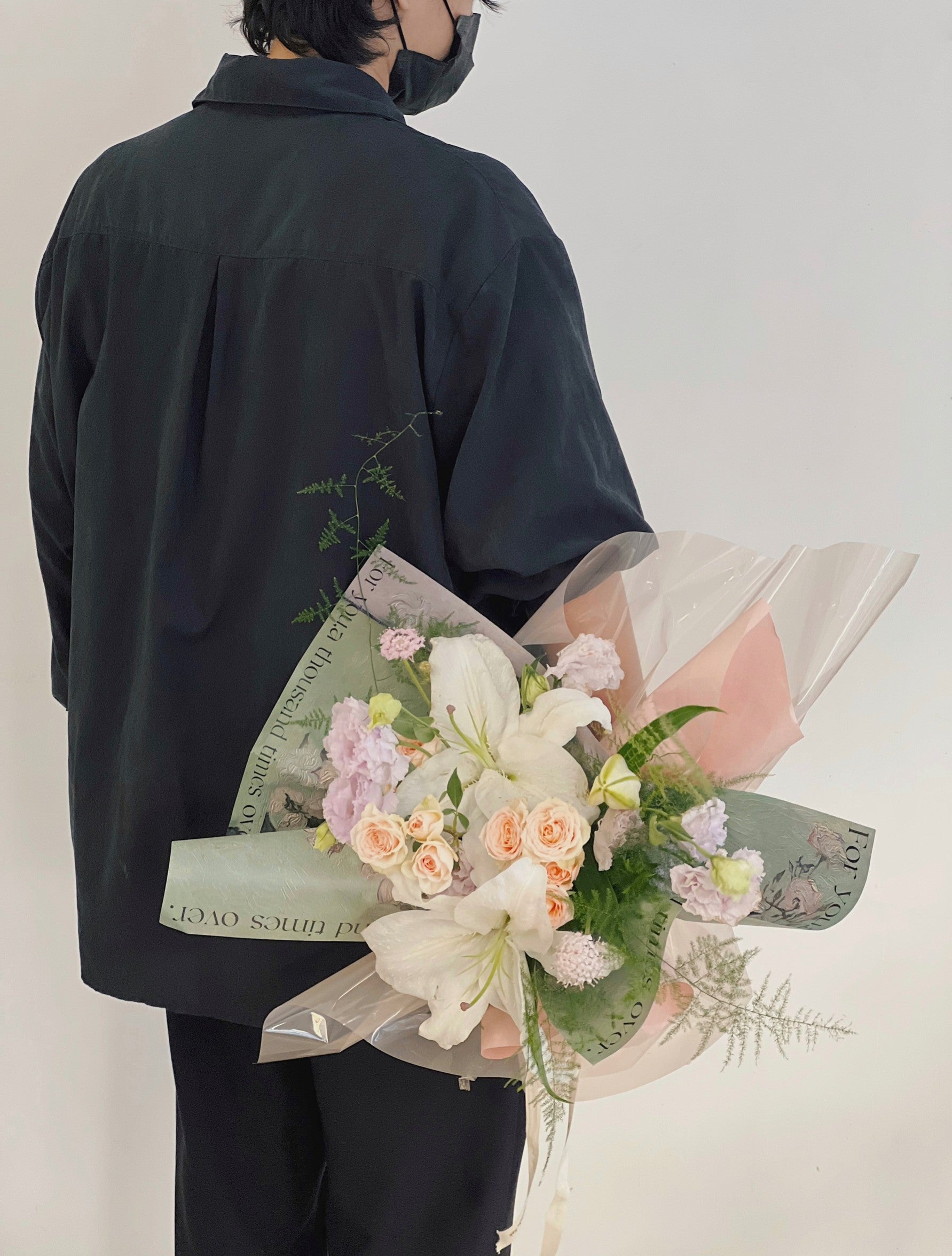 一位穿黑衣的持花者拿著百合花花束（綠色包裝）。